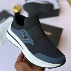 A hand holding a black and blue sneaker with a white sole, showcasing the shoe's sleek design and elastic strap.