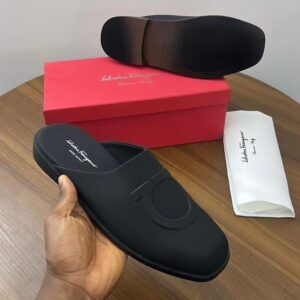 A pair of black satin Salvatore Ferragamo loafers on a wooden table with a red shoe box and white dust bag, showcasing the luxurious packaging and high-quality craftsmanship.