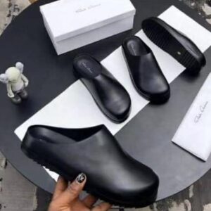 A pair of black leather clog shoes displayed on a table with a white box and cloth, perfect for comfortable and stylish footwear.