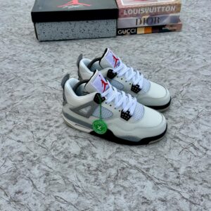 A pair of white and grey Air Jordan sneakers with a red logo, displayed on a marble surface with a shoe box and luxury brand books in the background.