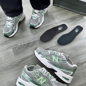 Luxury New Balance 574 sneakers in grey and green, showcased with box and insoles on a wooden floor, perfect for high-class individuals in Nigeria.