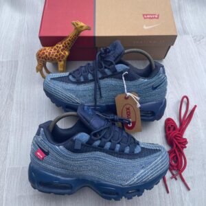 A pair of luxurious Nike Air Max sneakers in denim blue, displayed with a red shoe box and a giraffe figurine, showcasing high-class style and comfort.