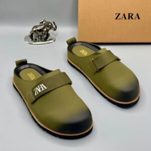 A pair of luxury green leather clogs with velcro strap and golden logo, displayed with a silver elephant statue and Zara box, showcasing high-class products for the elite at Levonteluxe in Nigeria.