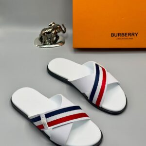 High-end white slides with red and blue stripes, displayed with Burberry box and golden elephant figurine on gray background, epitome of luxury footwear.