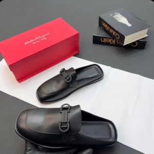 A pair of luxurious black leather mules with sleek buckles, accompanied by a red shoe box and luxury books, epitomizing high-end fashion.