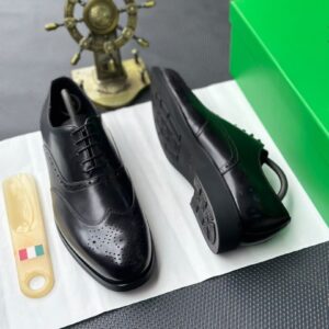 A pair of luxurious black leather oxford shoes with brogue detailing, accompanied by a shoe tree and presented on a premium white cloth, evoking a sense of high-end style and refinement.